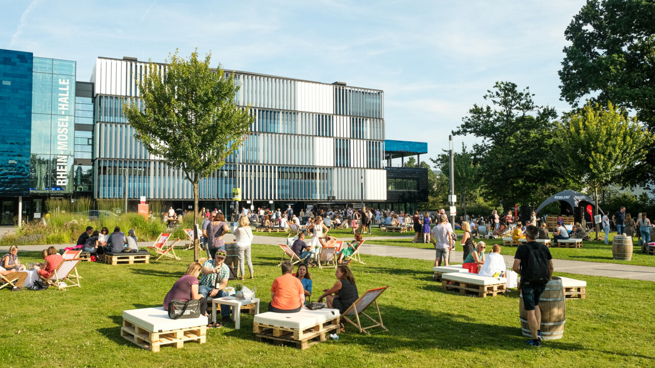 Menschengruppen sitzen verteilt bei der Blaue Stunde vor der Rhein-Mosel-Halle © Camaze